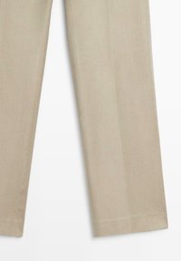 Spodní část béžových kalhot s rovnými nohavicemi a prošitými lemy na bílém pozadí.