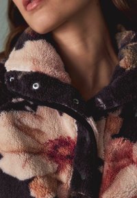 Virágmintás polárdzseki puha tapintású anyagból. Magas gallérral, patentokkal és sötét valamint pasztell színek keverékével rendelkezik.