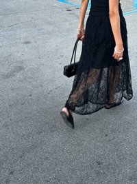 Black lace maxi skirt with sheer overlay and floral pattern, paired with a fitted black top and small black handbag. Walking on pavement.