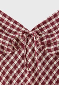 Tissu à carreaux rouge et blanc avec un nœud noué et des bords froncés, mettant en valeur la zone de l'encolure d'un vêtement.