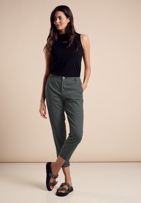 Top senza maniche nero a coste abbinato a pantaloni a quadri verdi, con chiusura a bottoni, tasche laterali e sandali neri con cinturini.