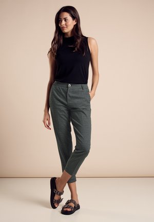 Top sans manches noir à côtes avec un pantalon à carreaux verts, comprenant un devant à boutons, des poches latérales et des sandales noires à lanières.