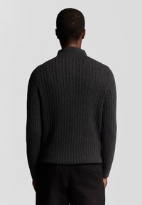 Donkergrijze geribbelde trui met een kraaghalslijn, voorzien van een gestructureerd oppervlak en aansluitende mouwen, weergegeven vanuit de achterkant.