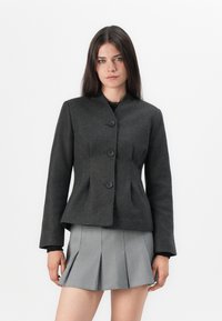 Chaqueta ajustada gris oscuro con un alto cuello, cuatro botones y cintura estructurada. Diseño ajustado con mangas largas. Complementada con una falda gris plisada.