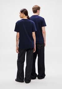 Camisetas de algodón azul marino de manga corta, con corte cuadrado, vistas desde atrás, combinadas con pantalones vaqueros oscuros, con detalles sutiles de costura.