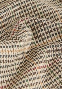 Tessuto con una base beige e un motivo pied-de-poule in marrone, verde e accenti rossi; morbido al tatto con dettagli di tessitura visibili.
