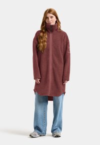 Bordeaux fleece jas met hoge kraag en een volledige rits, met lange mouwen en zijsplitten, gecombineerd met losse blauwe jeans en sneakers.