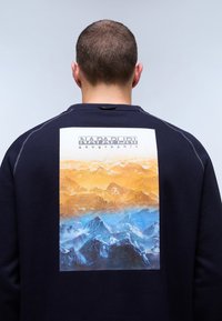 Felpa navy con una grande grafica di montagne con sfumature arancioni e blu. Logo "NAPAPIJRI geographic" stampato in alto.