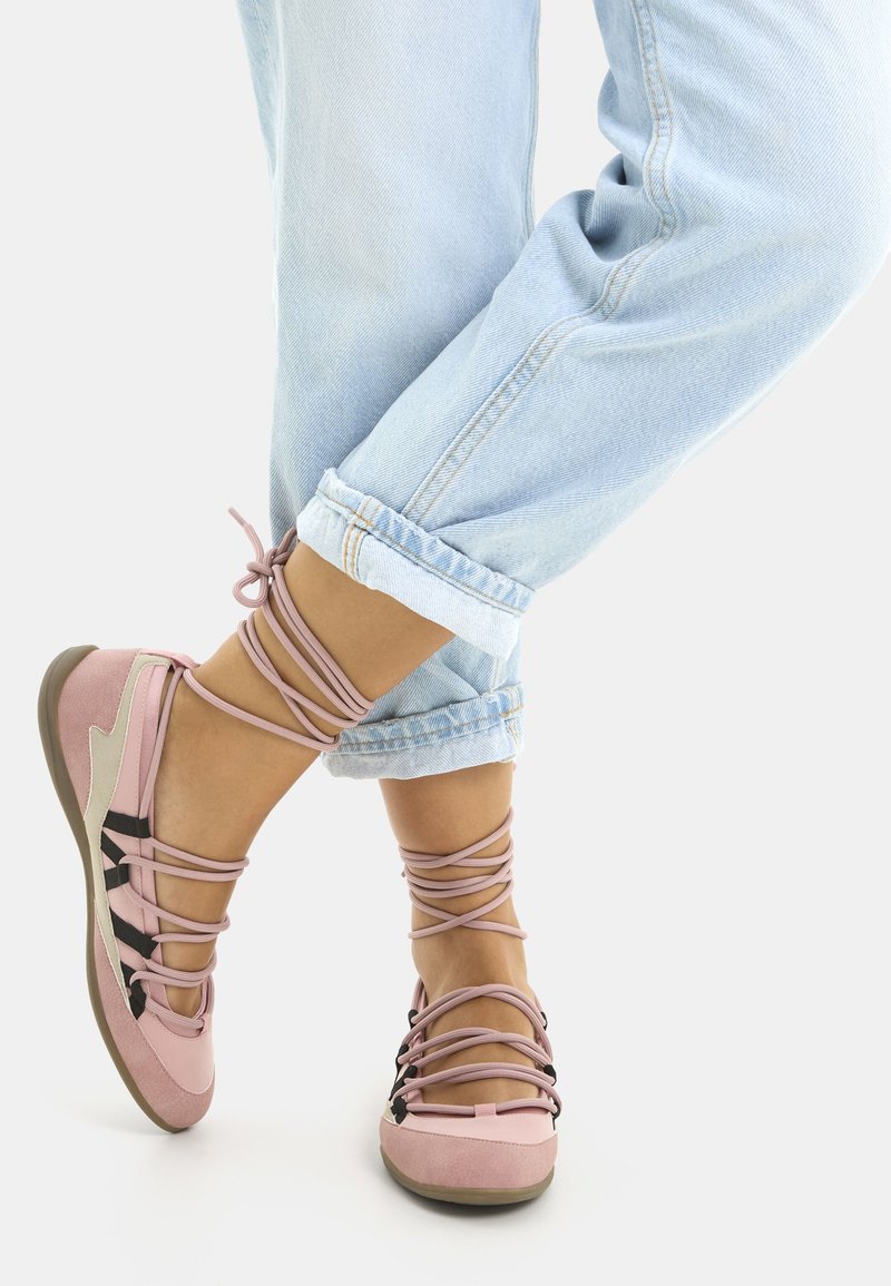 Zapatos rosa con cordones, de textura suave similar al ante, que presentan detalles negros y un talón gris. Llevados con jeans de color azul claro con los dobladillos enrollados.