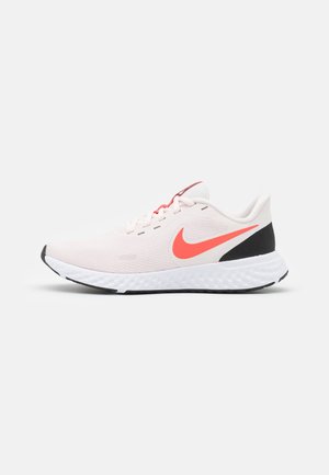 Zapatilla de running Nike de color rosa claro con el símbolo Swoosh en naranja brillante, suela blanca texturizada, talón negro y cordones a juego en naranja sobre fondo blanco.