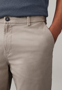 Beige chinos ar gludu tekstūru, ar pogu aizdari un sānu kabatām. Valkāti ar rakstainu tumši zilu kreklu.