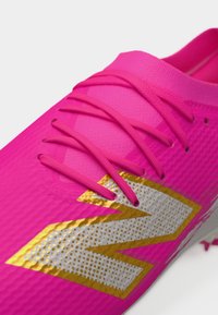 Scarpa sportiva di un vivace rosa con lacci abbinati e un grande logo "N" in argento e oro sul lato.