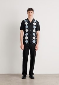Chemise noire à manches courtes avec un motif en losanges bleu clair et blanc, assortie à un pantalon noir et des chaussures noires. Design simple à boutons.