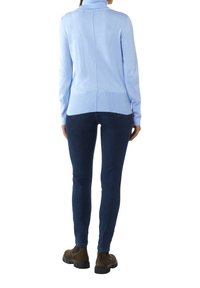 Jasnoniebieski sweter z golfem, wykonany z miękkiego materiału dzianinowego, z rozcięciem na dole, zestawiony z ciemnogranatowymi skinny jeansami i brązowymi botkami na kostkę.