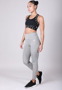 Soutien-gorge de sport noir avec une bande logo, associé à un legging gris taille haute avec des accents en maille et une coupe ajustée. Chaussures de sport noires.