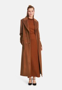 Brown wool blend coat with a tailored fit, large collar, double-breasted design, and side pockets. Worn over a matching brown dress.