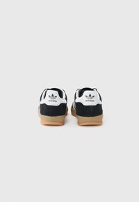 Sort ruskindssneakers med hvide accenter og branding, prydet med en gummirådgulv og tre striber på siden.