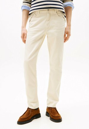 Beige katoenen broek met een slim fit, voorzien van zakken aan de zijkanten en een tailleband met lussen voor een riem, gecombineerd met bruine suède schoenen.