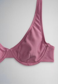 Pink ribbed fabric bra with underwire and wide shoulder strap, shown flat on a neutral background.