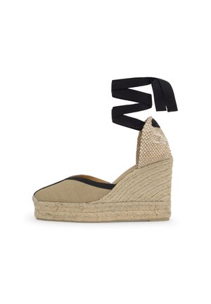 Zapato cuña espadrille beige con suela de yute tejido, punta cerrada, ribete negro y lazadas de tela negra que se atan alrededor del tobillo.