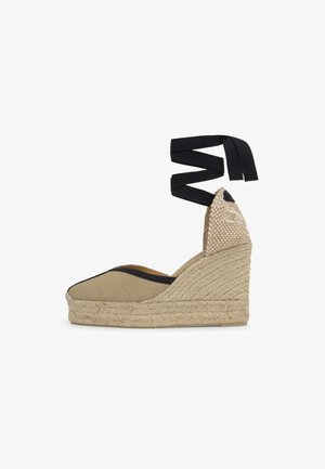 Zapato cuña espadrille beige con suela de yute tejido, punta cerrada, ribete negro y lazadas de tela negra que se atan alrededor del tobillo.