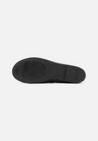 Semelle de chaussure noire avec une texture lisse, comportant une section de grip à motifs et un talon rectangulaire distinct. Design simple sans embellissements.