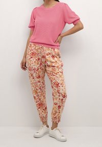 Roze textuur kortemouwen trui gecombineerd met lichtgewicht joggerbroek met bloemenpatroon; voorzien van een elastische tailleband en witte sneakers.