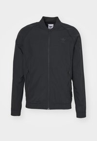 Svart zip-up jacka i lätt tyg. Har ståkrage, elastiska ärmslut och sidofickor, med en diskret logotyp på bröstet.