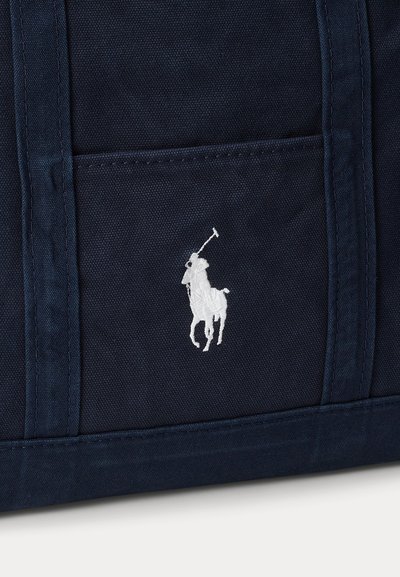 Sac en tissu bleu foncé avec poche avant et logo blanc brodé représentant un joueur de polo à cheval tenant un maillet.