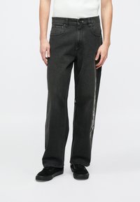 Svarta jeans i denim med lös passform, utrustade med en knäppning framtill och sidfickor, dekorerade med en vit grafisk design på benet.