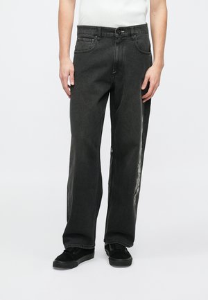 Czarne dżinsy z denimu o luźnym kroju, z zapięciem na guziki z przodu i kieszeniami po bokach, ozdobione białym graficznym wzorem na nogawce.