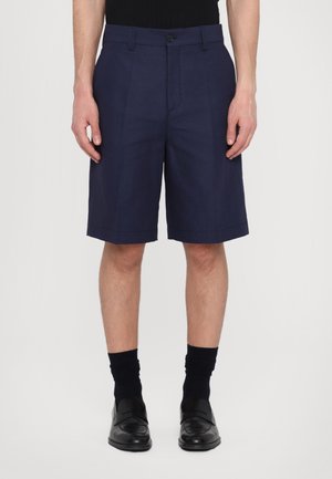 Marineblaue Shorts mit maßgeschneiderter Passform, versehen mit Falten und einem einzelnen Knopfverschluss. Hergestellt aus einem strukturierten Stoff, der knapp über dem Knie endet.