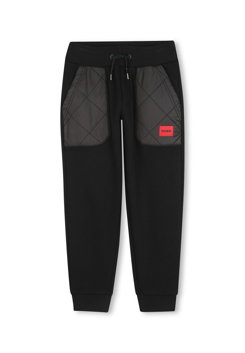 Zwarte trainingbroek met gewatteerde grijze zijzakken, elastische tailleband en trekkoord. Voorzien van een rood logo label op de rechterzak.