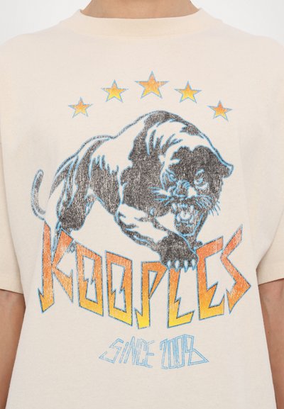 Kremfarget bomull T-skjorte med grafikk av en svart panter, oransje og blå "KOOPLES" tekst, og fem gule stjerner over designet.