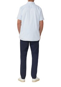 Camicia azzurro chiaro a maniche corte con colletto a punta e yoke posteriore; abbinata a pantaloni navy e sneakers bianche, vista da dietro.