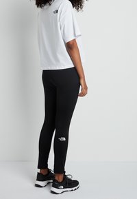 Black leggings with a white logo on the ankle, paired with a cropped white t-shirt. The outfit features a simple design and fit.