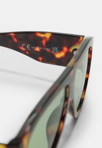 Occhiali da sole tartarugati con lenti verdi, realizzati in plastica. Caratteristiche includono un design elegante e incisioni sul terminale.