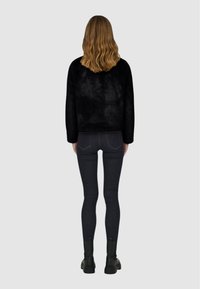 Schwarzer, flauschiger Pullover, von hinten gesehen, kombiniert mit dunklen Jeans und schwarzen Stiefeletten. Gerader Schnitt und schlichtes Design.