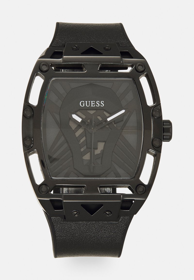 Must друзей дизаин черная Guess часовидет с прямоугольным корпусом с вырезанными деталями, текстурированным черным кожаным ремешком и узорчатым темным циферблатом с серебряными стрелками.