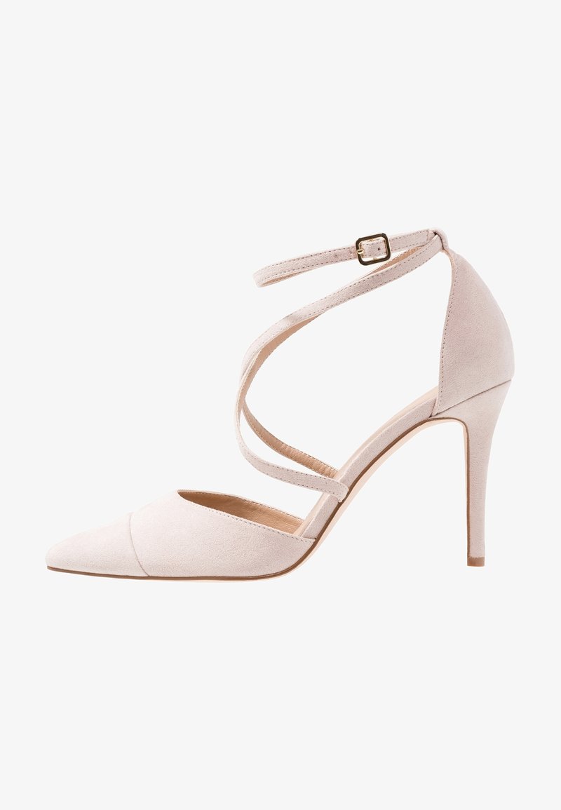 Chaussure à talon haut beige avec bout pointu, talon aiguille fin, brides entourant la cheville et petite boucle dorée sur la bride de cheville.