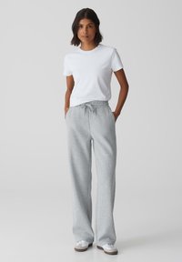 Lichtgrijze sweatpants met een trekkoord in de taille, met een ontspannen pasvorm en zijzakken, gecombineerd met een eenvoudig wit T-shirt en witte sneakers.