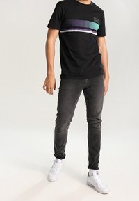 Svart bomulls t-shirt med ett horisontellt gradientrand i turkos, lila och vitt. Kombinerad med grå slim-fit jeans och vita sneakers.