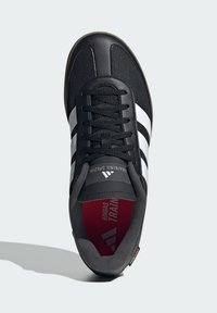 Black athletic shoe with a synthetic upper, three white stripes, and red interior. Features a lace-up design and a textured rubber sole.