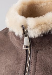Brown suede jacket with a cream faux fur collar, featuring a silver zipper and visible stitching detail along the seams.