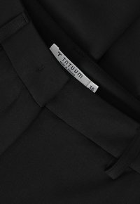 Primo piano di un garbamento nero con passanti per cintura e etichetta bianca con la scritta "TNTUUM, Made in Poland, taglia 36."