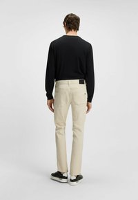 Beige cotton trousers with a straight fit and rear pockets, paired with a fitted black long-sleeve shirt and black sneakers.
