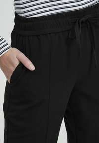 Črne športne hlače z vrvico v pasu, stranskimi žepi in mehkobo materiala. Povezane z dolgim majicom z odsekom na pasu v črtastem vzorcu.