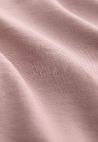 Zbliżenie miękkiej, jasnofioletowej tkaniny ukazującej drobną dzianinową teksturę i delikatne fałdy.