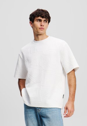 Biely textúrovaný krátky rukáv s embosovaným geometrickým vzorom, skombinovaný so svetlomodrými džínsami.