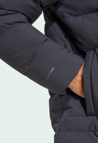 Dark blue puffer jacket with quilted texture, featuring a cuff with "CLIMAWARM" branding. The fabric appears smooth and weather-resistant.